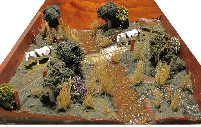 A diorama depicting an impaired stream after removal of sediment accumulations and installation of a vegetated riparian buffer and a designated livestock watering/crossing area.